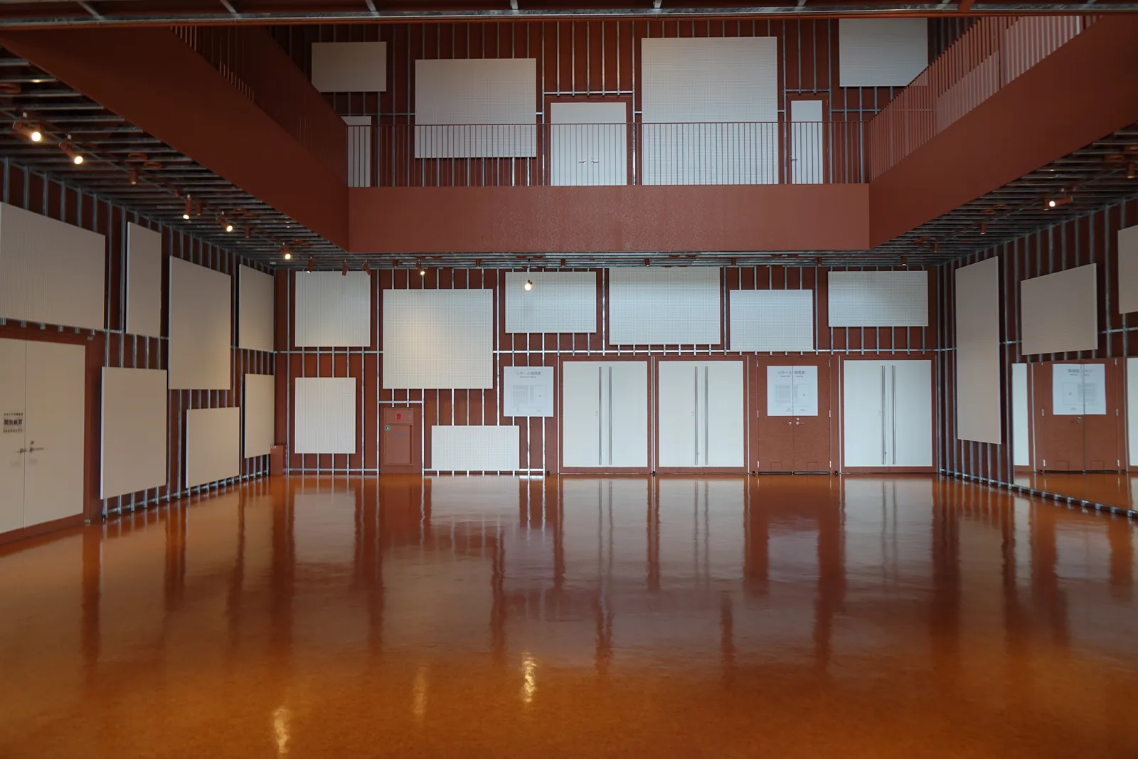 磚紅色牆面與橙褐色反光地坪，牆上排列白色方形吸音板，空間空曠