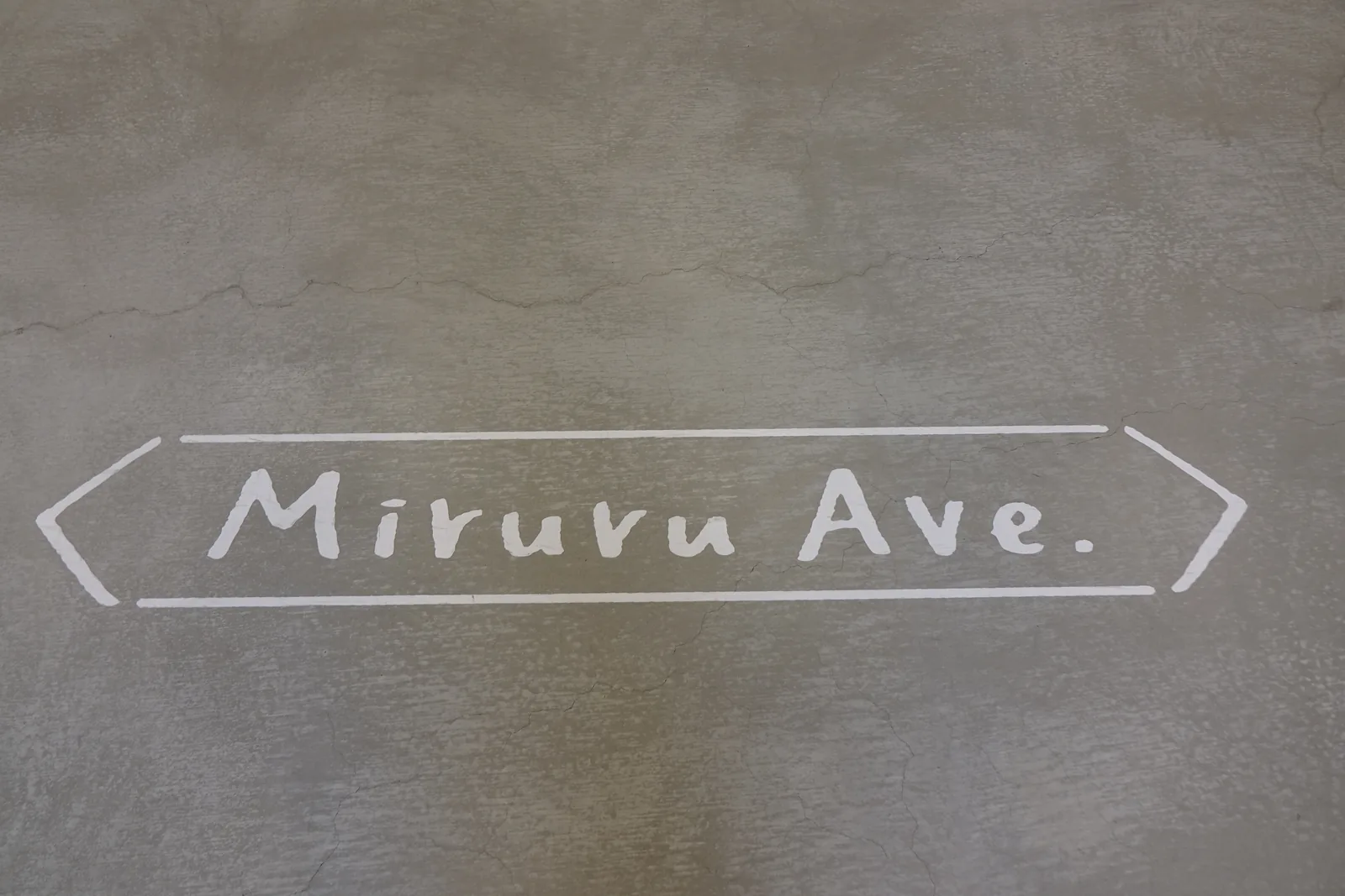 地坪的淺灰色粉刷面上，以白色手寫體寫著英文 Miruru Ave.，兩側以箭頭形的線框圍起