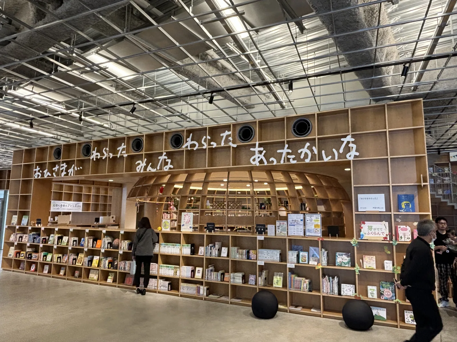 一樓兒童區的入口，一面木製書架上方以白色大字寫著一句話，書架中央開了一個拱形的開口，開口內是以曲線木條圍成的圓形空間，書架下方擺著黑色的球形坐墊