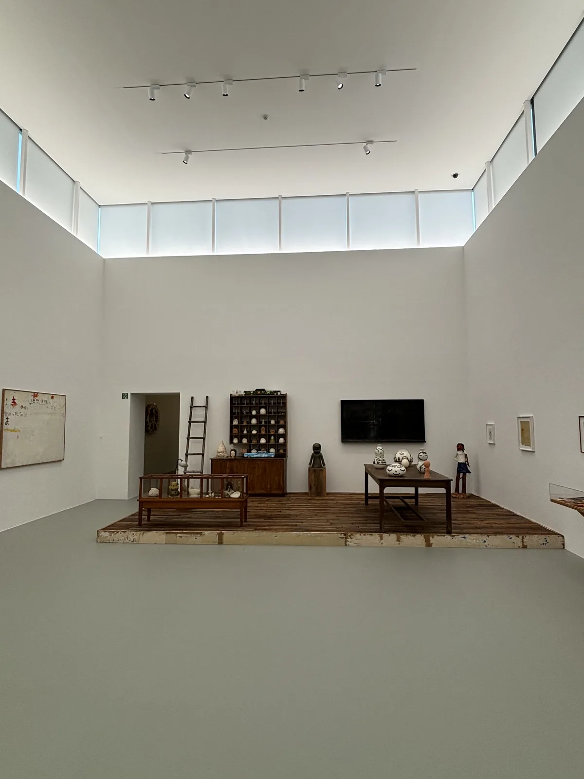 展示室四的中央，一塊以舊木板拼成的低平台上放著一座木製玻璃展示櫃、一座小格子木櫃、一架木梯與一座人像雕塑，後方的白牆上掛著一台螢幕，牆上方是高側窗