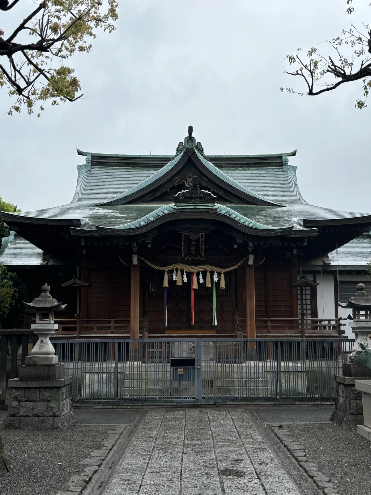 町田天滿宮的拜殿，木造的建築上覆綠色的金屬屋面，正面懸掛注連繩與彩色布條，前方是石板參道與石燈籠