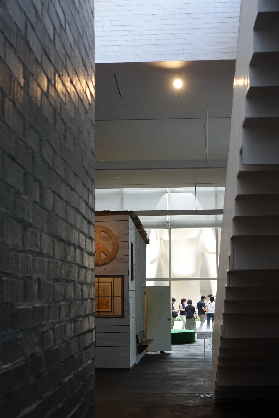 多層次空間：灰色清水磚牆、白色階梯與白色木作小屋狀展示結構並置，遠處落地玻璃可見青森犬局部