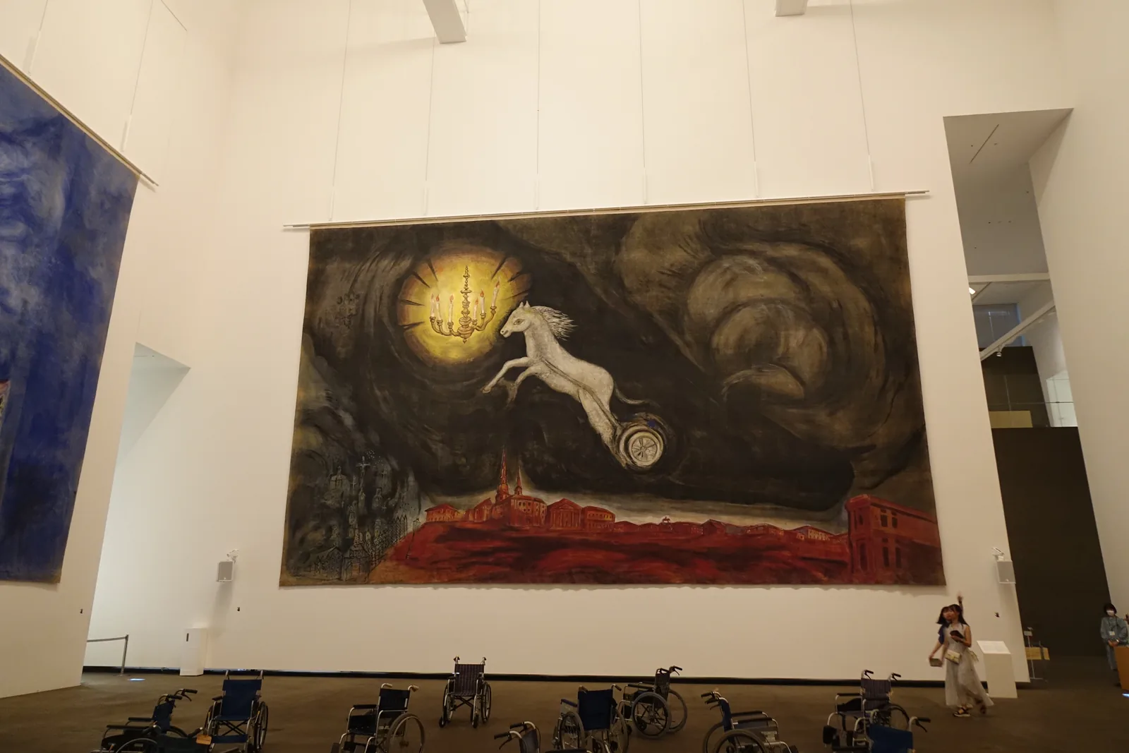 Aleko Hall室內全景，挑高四層樓白色大廳，牆面懸掛夏卡爾巨幅背景畫，畫作下方地面排列輪椅，天花外露樑架