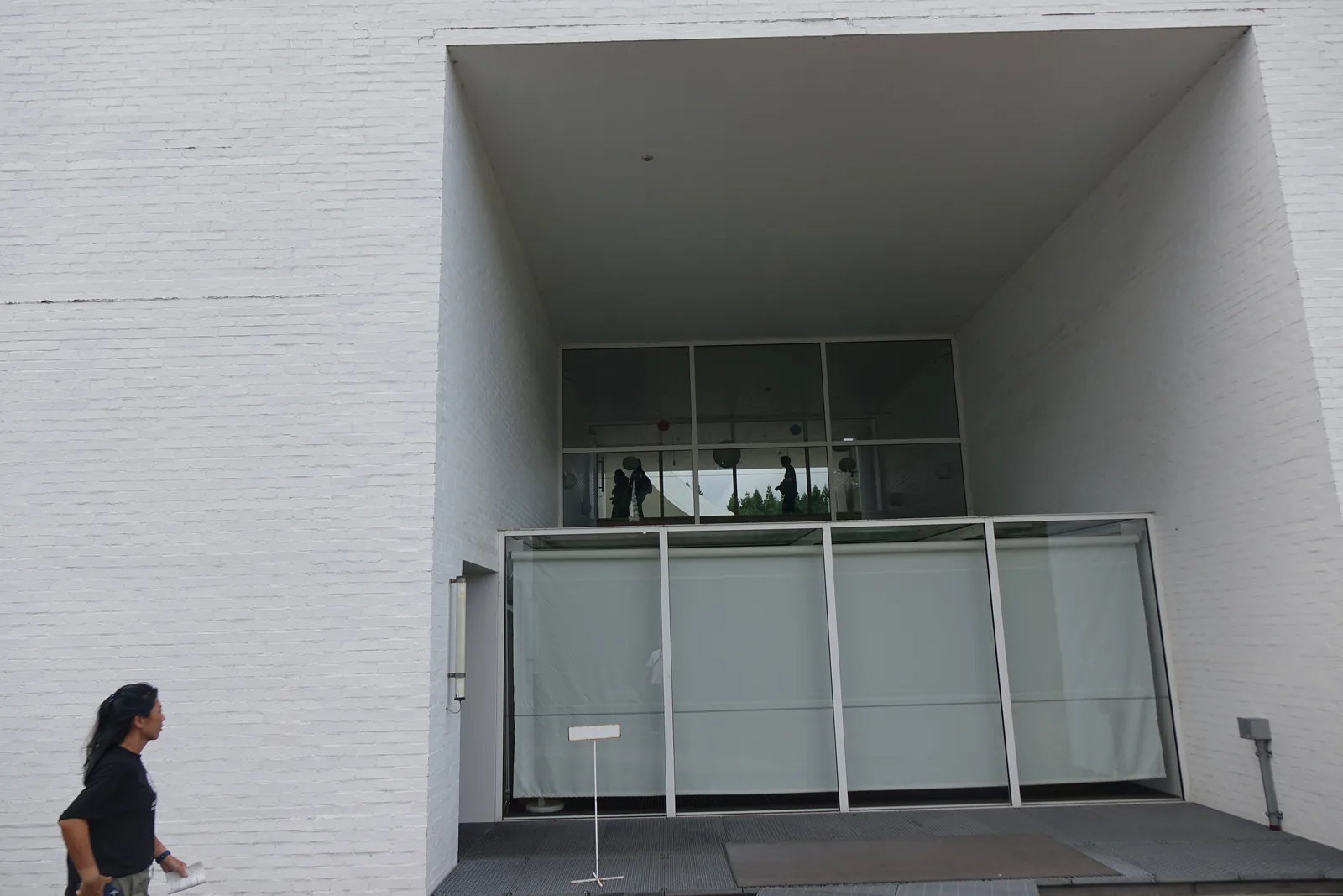 白色牆面上挖出的深方形開口，開口內為玻璃門與扶手，左側一名人物作為尺度
