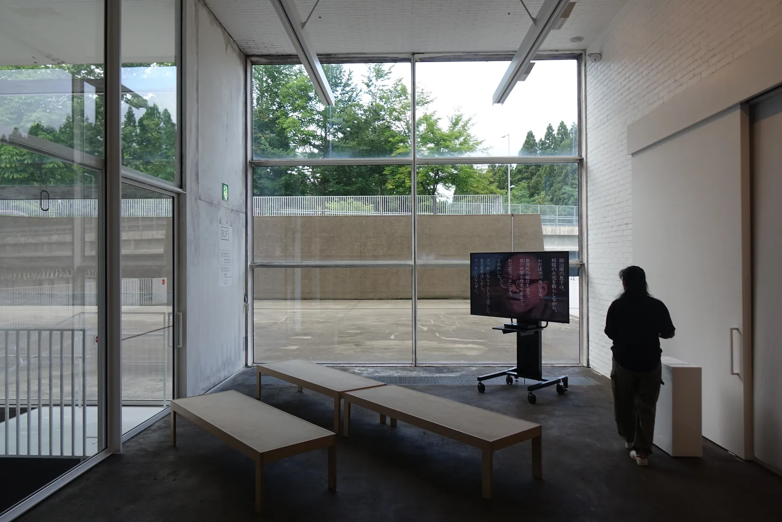 展示室一角的大片玻璃，窗外為草坪與溝渠的土牆，室內置有長凳與螢幕