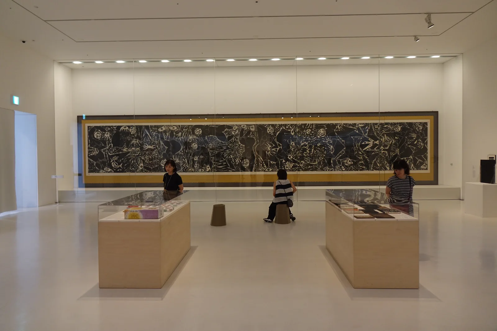 棟方志功展示室，牆上懸掛一幅巨大的橫長版畫，前方為兩座展示台，地面淺色