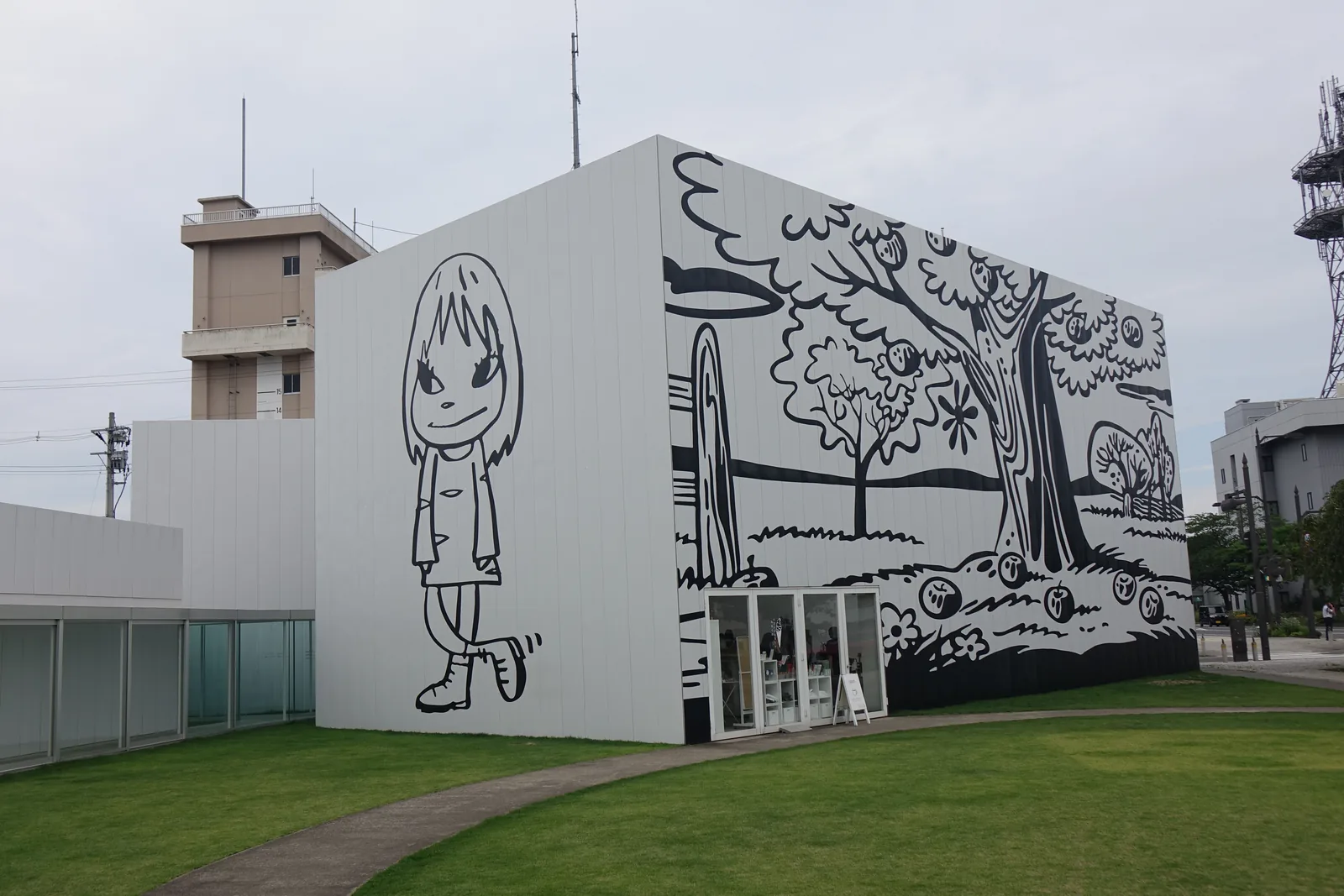 白色方盒外牆上的巨大線描女孩與蘋果樹原野，牆腳開一組玻璃門