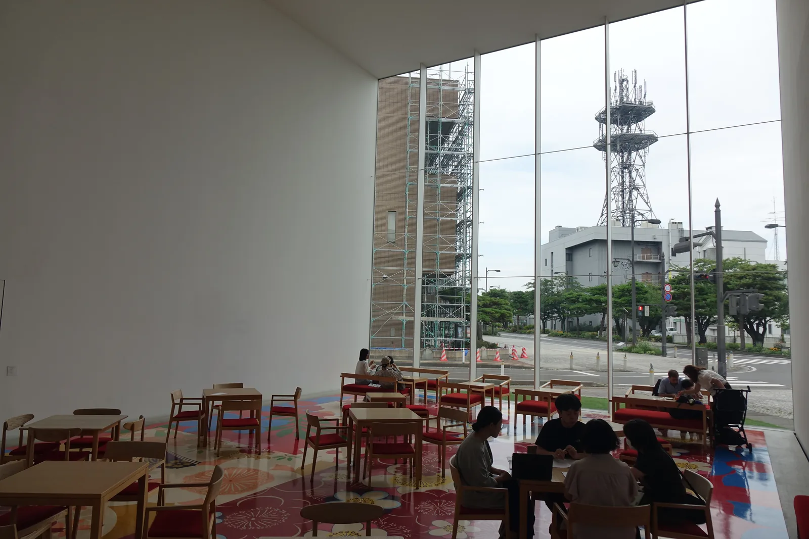 咖啡館：白牆直上高處，通高落地玻璃外是街口與電信鐵塔，地面為大朵花卉圖案