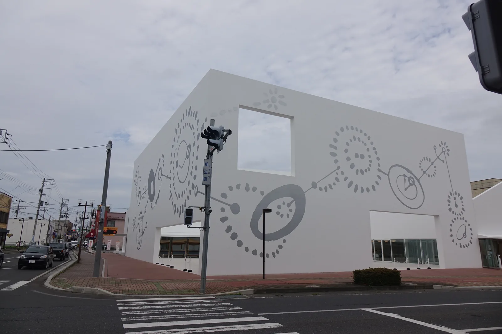 十和田市地域交流中心的白色山牆，開著兩個方形大開口，牆面上是灰色點與圈的壁畫