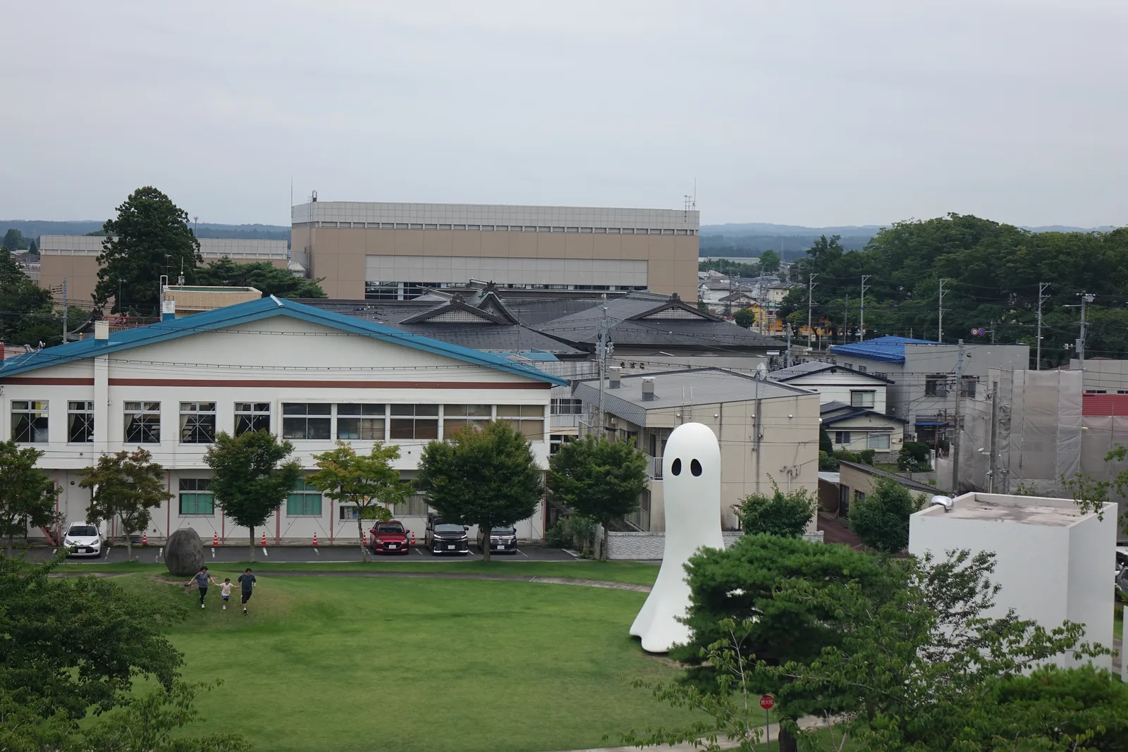 自屋頂平台俯瞰十和田市街，前景為樹木與草坪，遠處為低層建築與學校