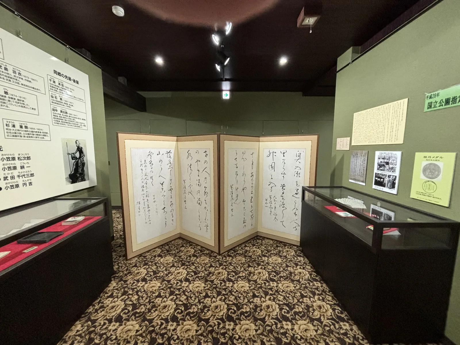 大町桂月資料館：墨綠色牆面、深色天花與花紋地毯，中央為一座書法屏風，兩側為展示櫃