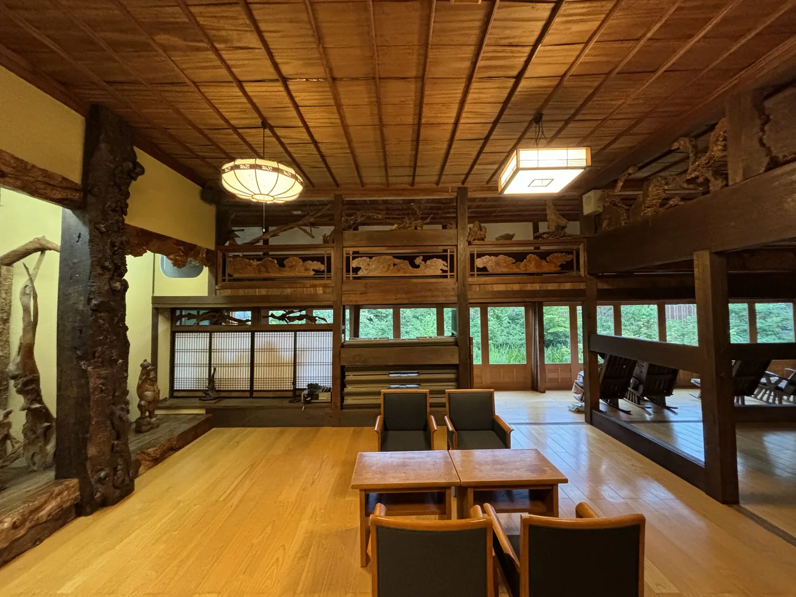 大廳前區，格子天花下垂吊方形燈具，木桌椅排列，後方為欄間雕刻與窗