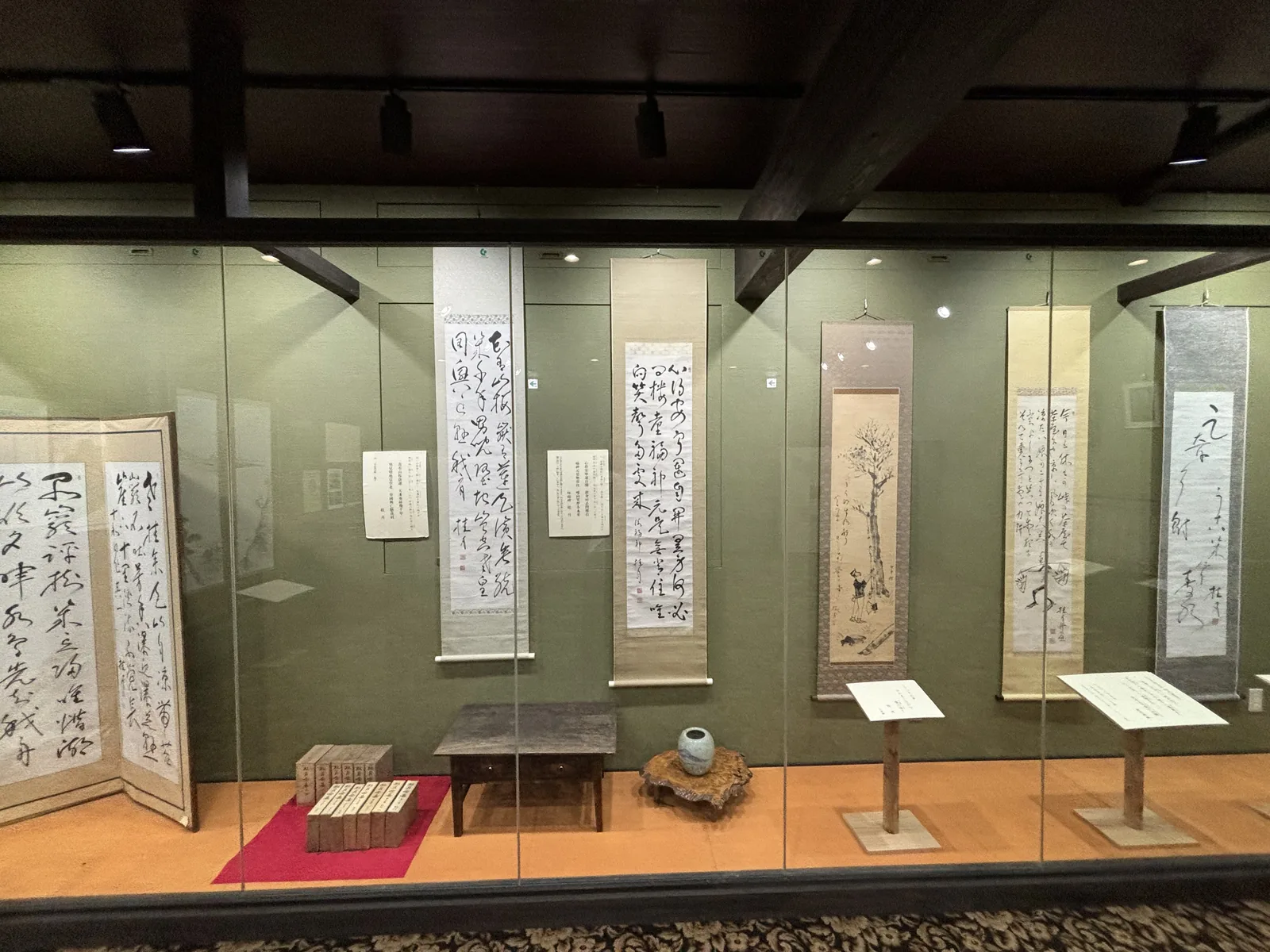 資料館內的玻璃展示櫃，墨綠色牆面前陳列數幅書法掛軸，下方置有展示台