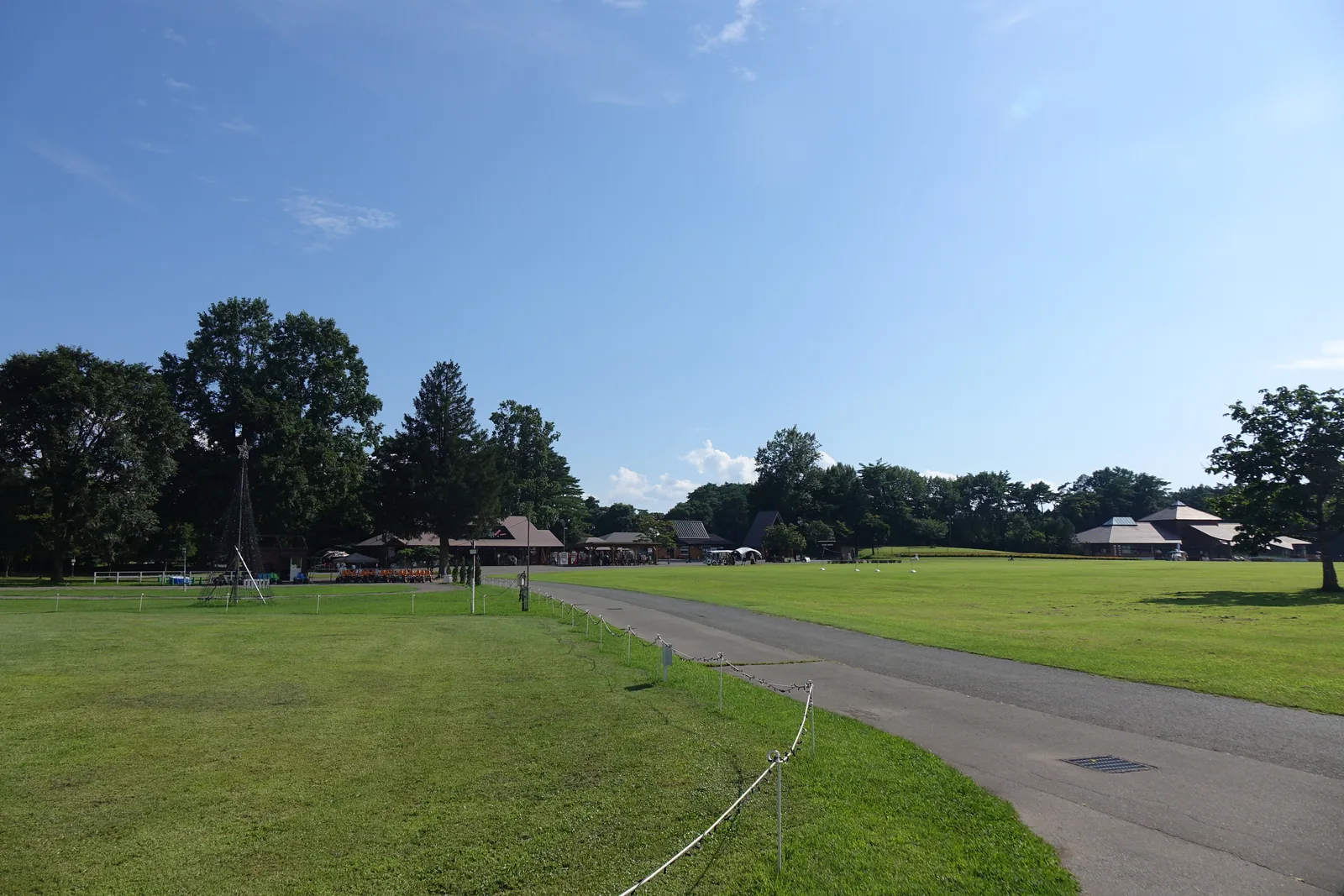 園內步道：步道兩側為草地，盡頭沿樹林帶排列著深色斜屋頂的低層建築