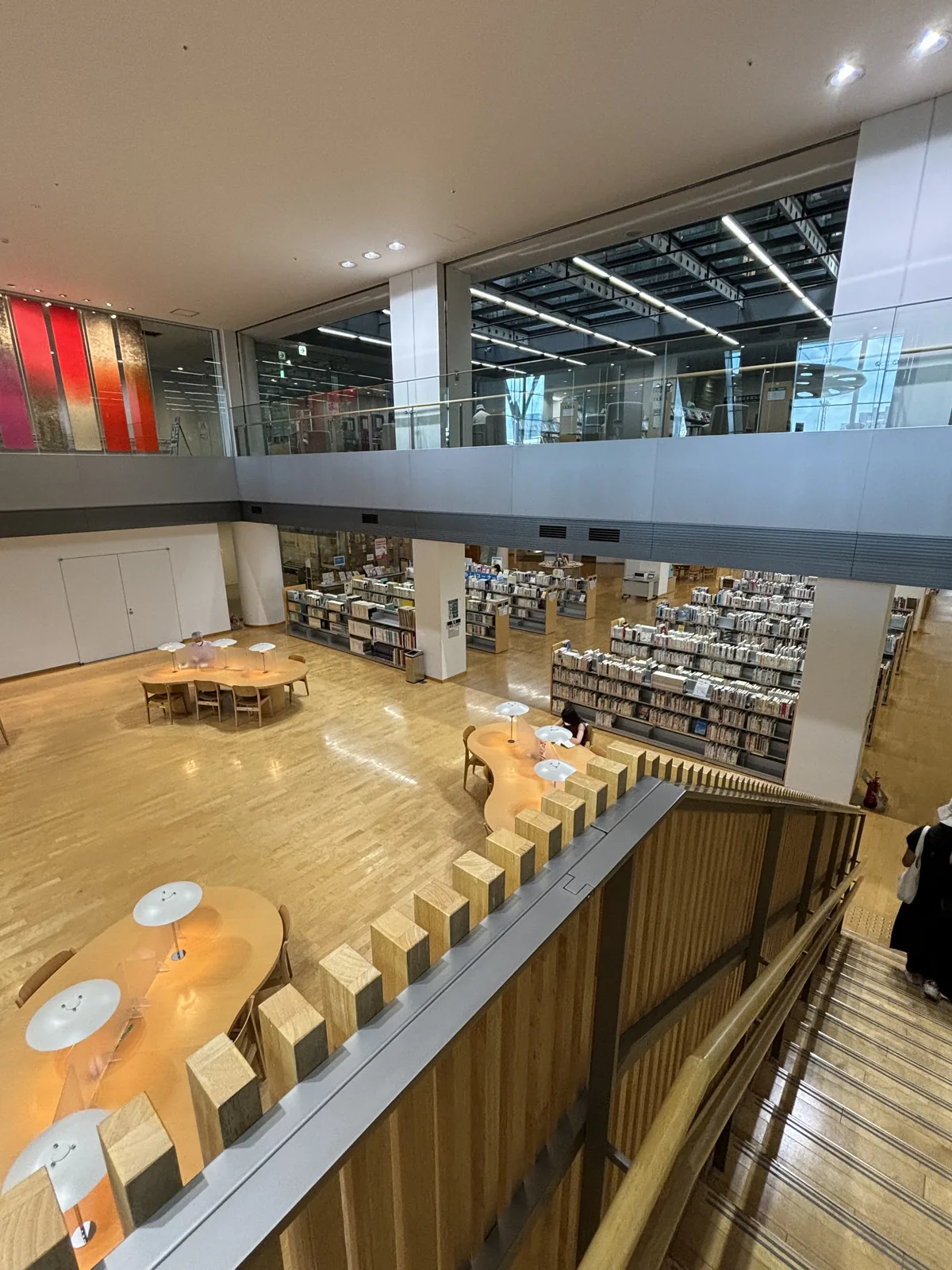 圖書館四樓俯視三樓閱覽區：兩層挑空，淺色木地板上散置流線形閱覽桌