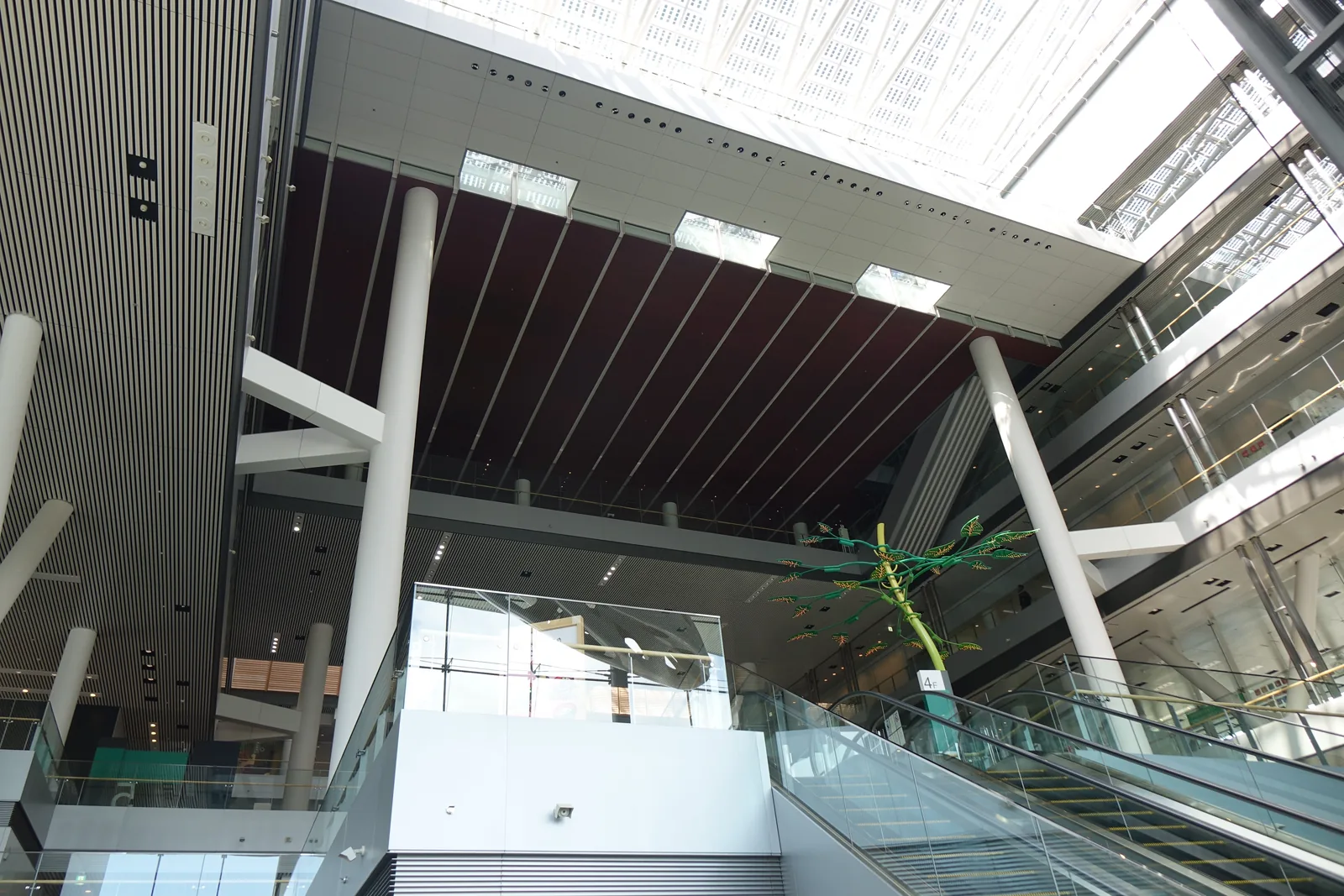 中庭內部，白色斜柱撐起上層樓板，一側為電扶梯，上方為玻璃屋頂與深色天花