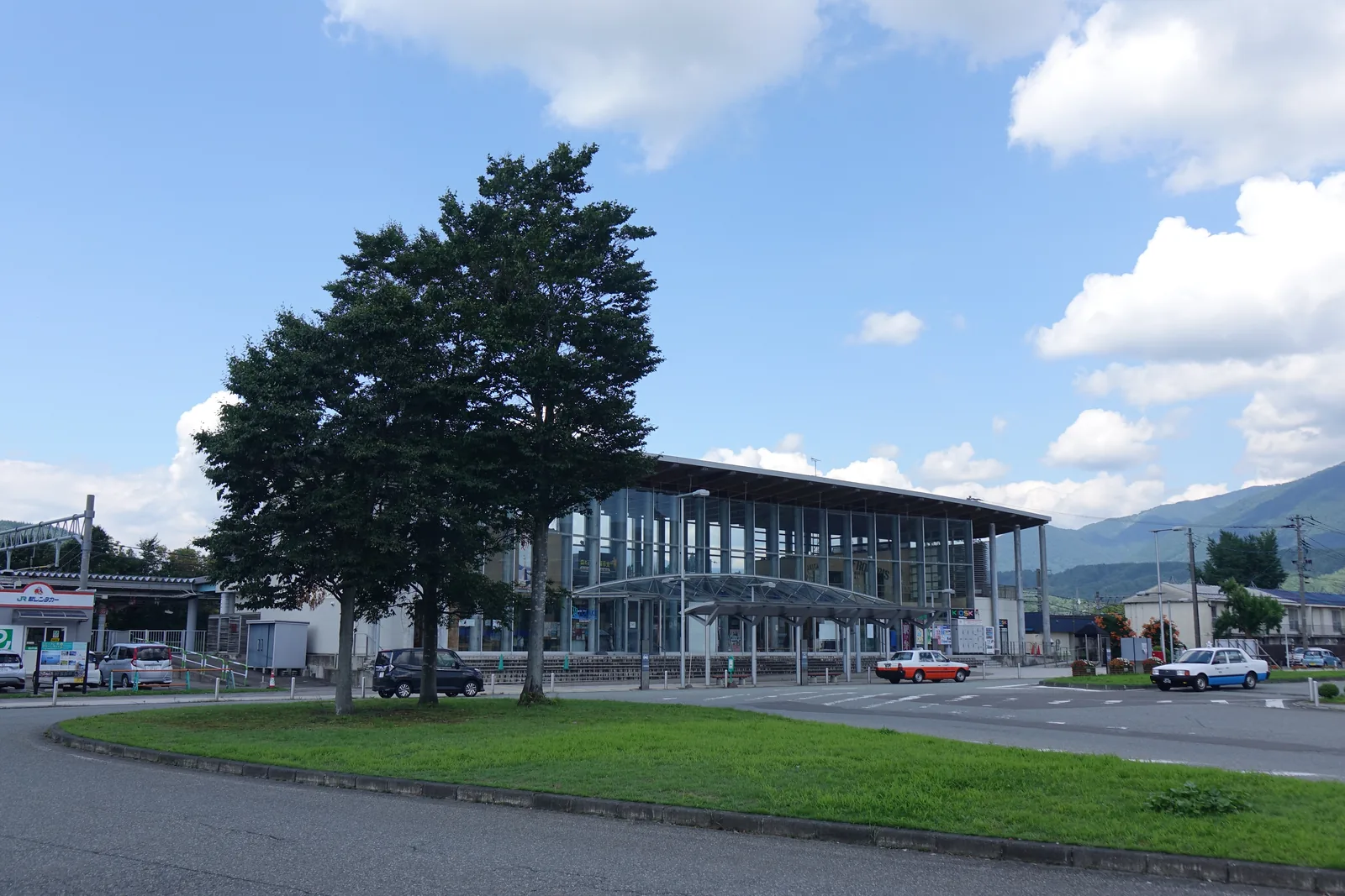站前廣場所見的田澤湖站：玻璃正面後方是成列的灰色圓柱，屋簷之後可見山脈