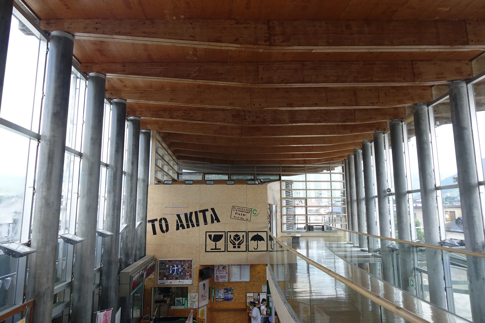 二樓迴廊：木地板迴廊、成列圓柱與玻璃牆，盡頭牆面寫著「TO AKITA」