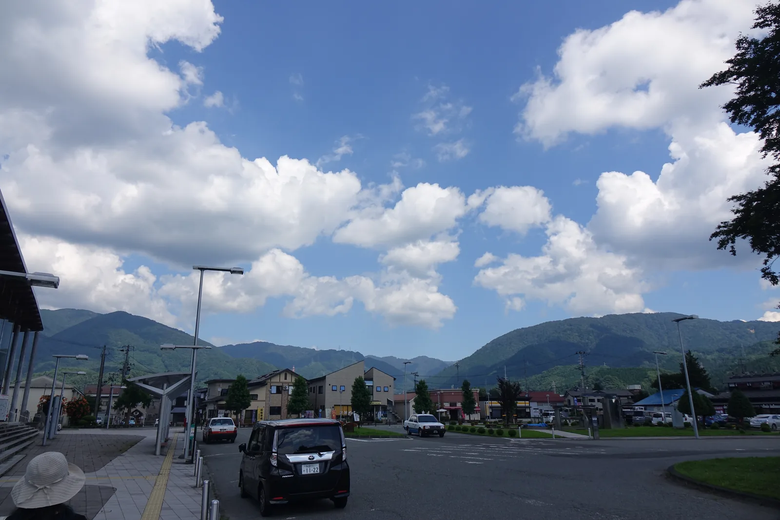 站前廣場一角，停車場與低矮街屋之後為連綿的山巒，天空晴朗有雲