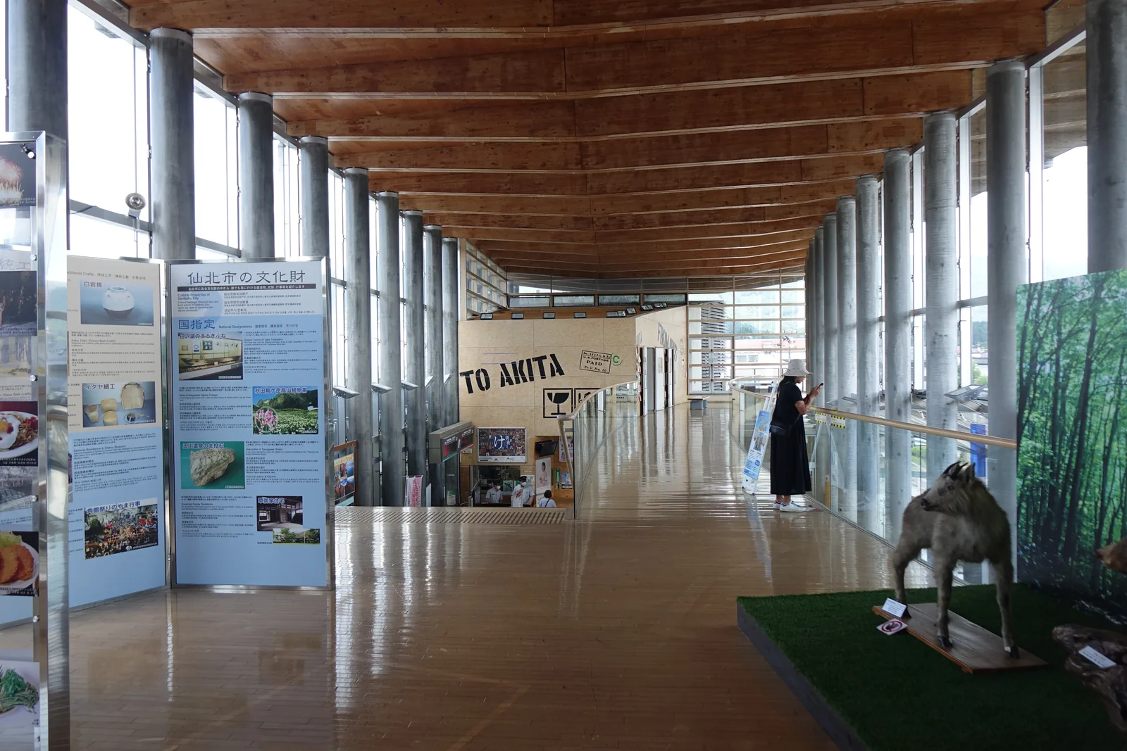 二樓的展示空間，木地板上擺放展示品，兩側為圓柱與展示板，屋頂梁在上方連續