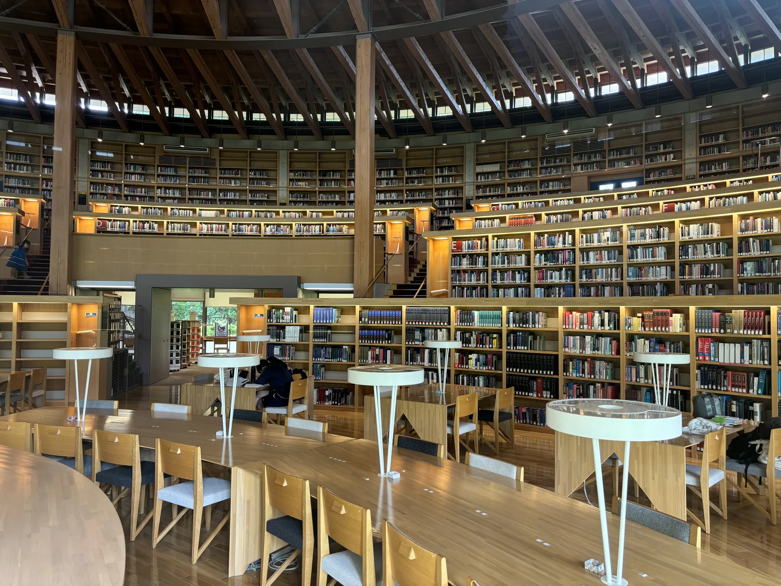半圓形閱覽廳全景，前景為弧形閱覽桌與白色桌燈，書架沿同心圓逐層升高，上方為放射狀杉木梁構成的傘形屋頂與一圈高側窗