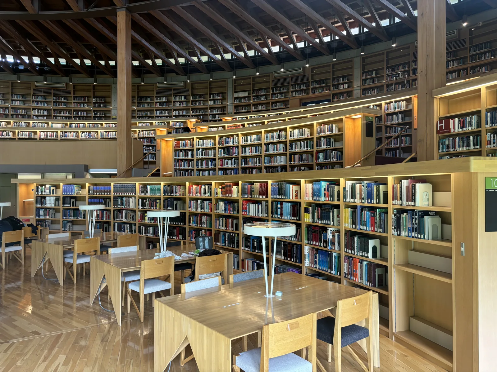 閱覽廳的近景，木製閱覽桌與椅子排列，後方為逐層升高的書架與傘形屋頂