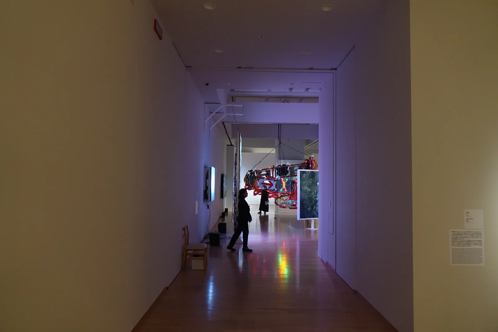 展示室之間的走廊，牆面反射紫色燈光，遠端為展示中的大型作品