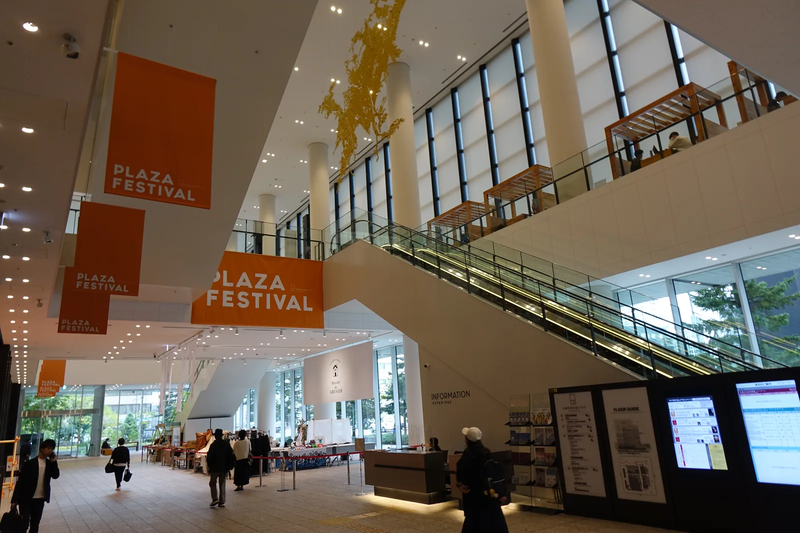 一樓 SCARTS mall 入口，左側懸掛橘色活動布旗，中央為服務台與數位看板，右側電扶梯與樓梯斜向上升，天花挑高