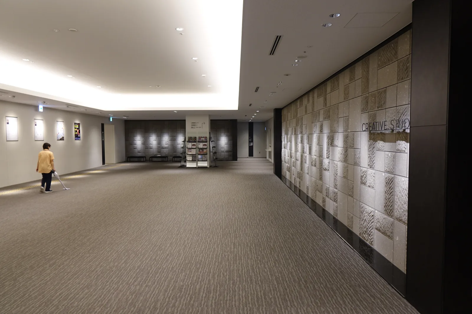 三樓 Creative Studio 前廳，右側為刻有斜向鑿紋的淺灰色石材牆，天花較低，地面鋪設灰色地毯，遠端牆上掛有海報