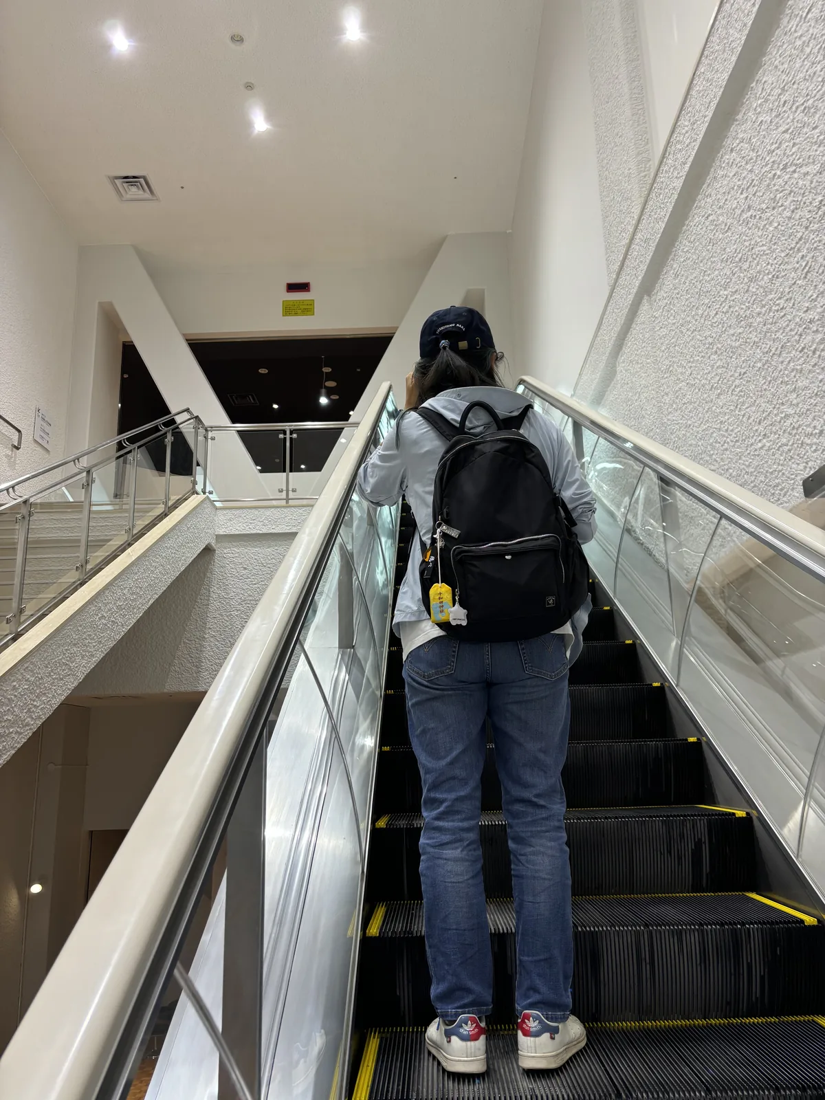 通往展示室的電扶梯，兩側為白色牆面與玻璃欄杆，上方為天花開口