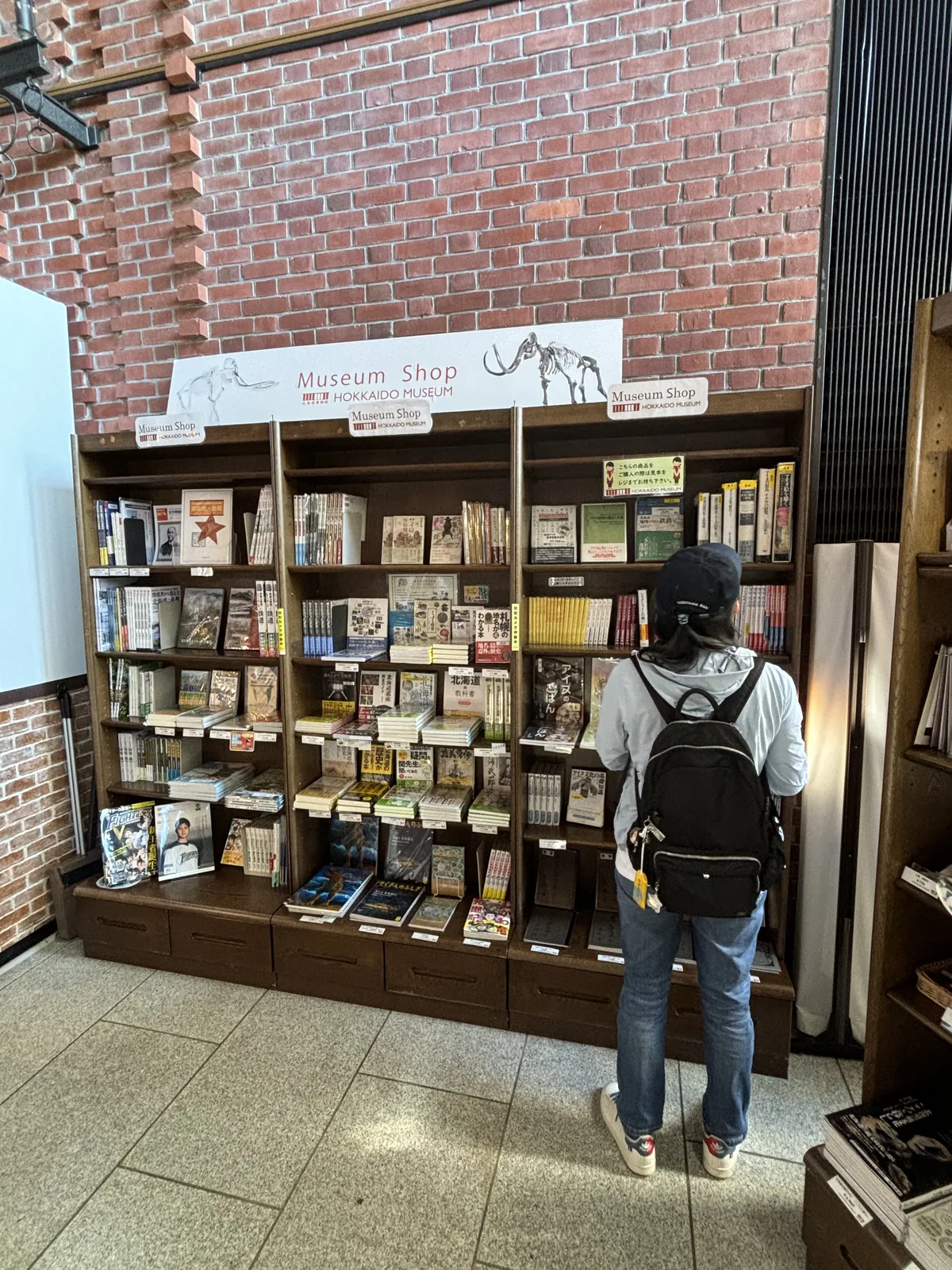 博物館商店的書架，紅磚牆面上掛著繪有長毛象骨骼的店招，木製書架上陳列書籍與出版物