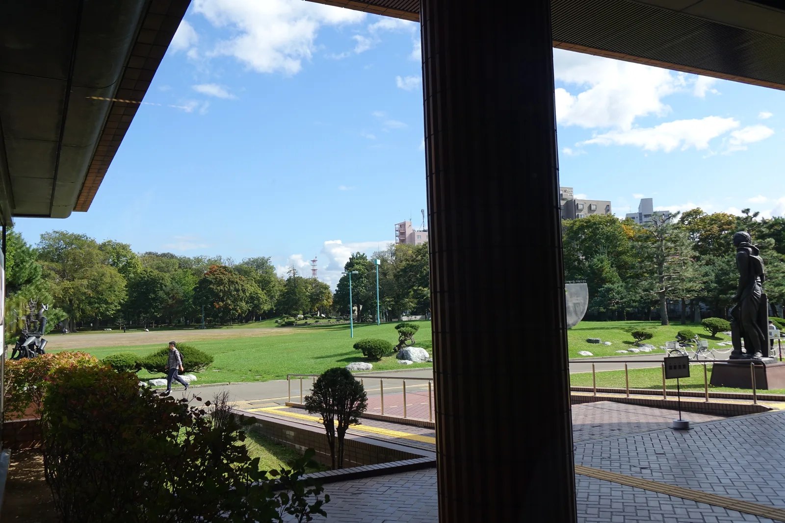 自大廳透過玻璃望向公園，深色圓柱將視野分成兩段，外面為草坪、樹林與館前的青銅雕像