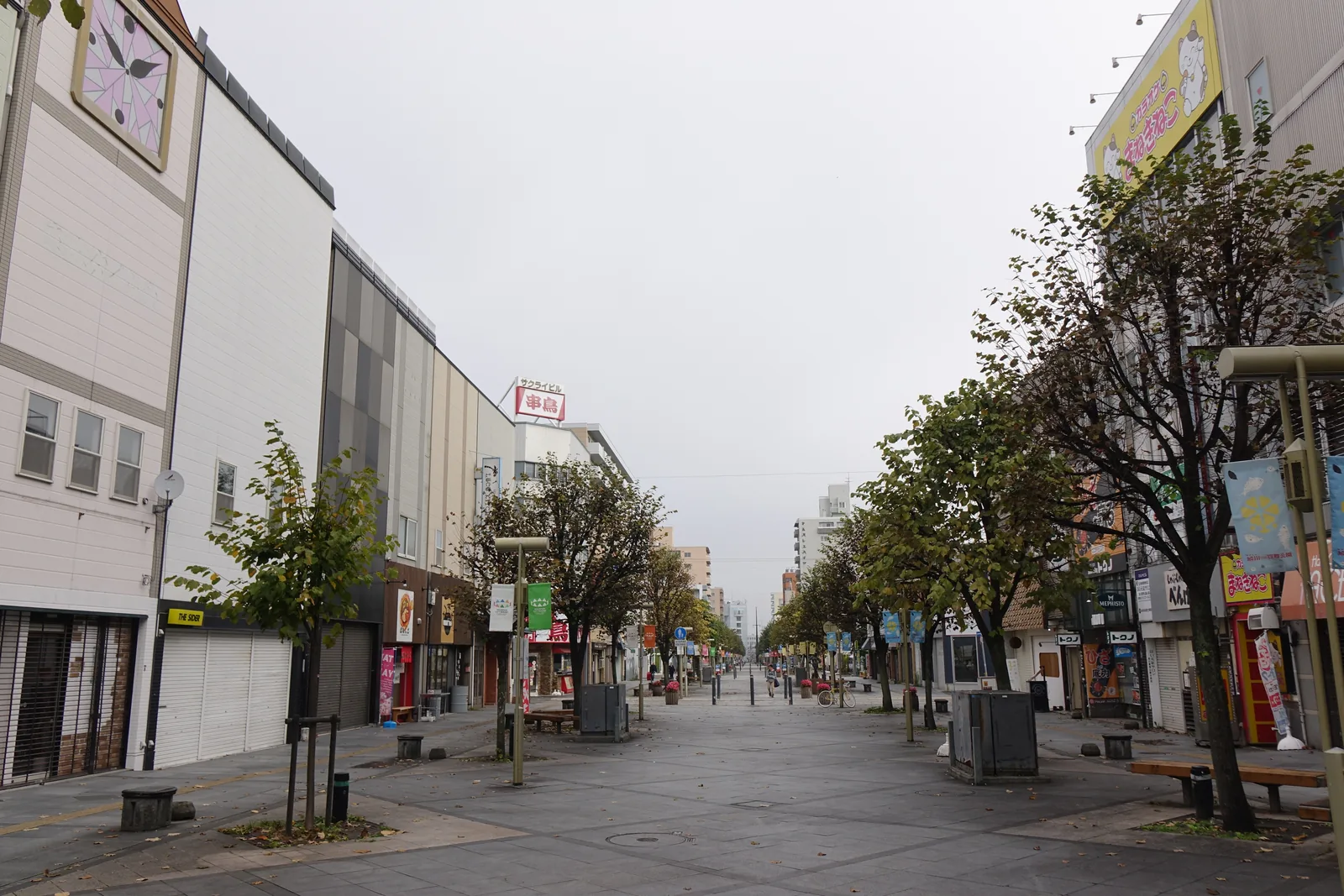 清晨的中心商業區步行街，兩側為商店與行道樹，街上幾乎無人，遠處為高樓