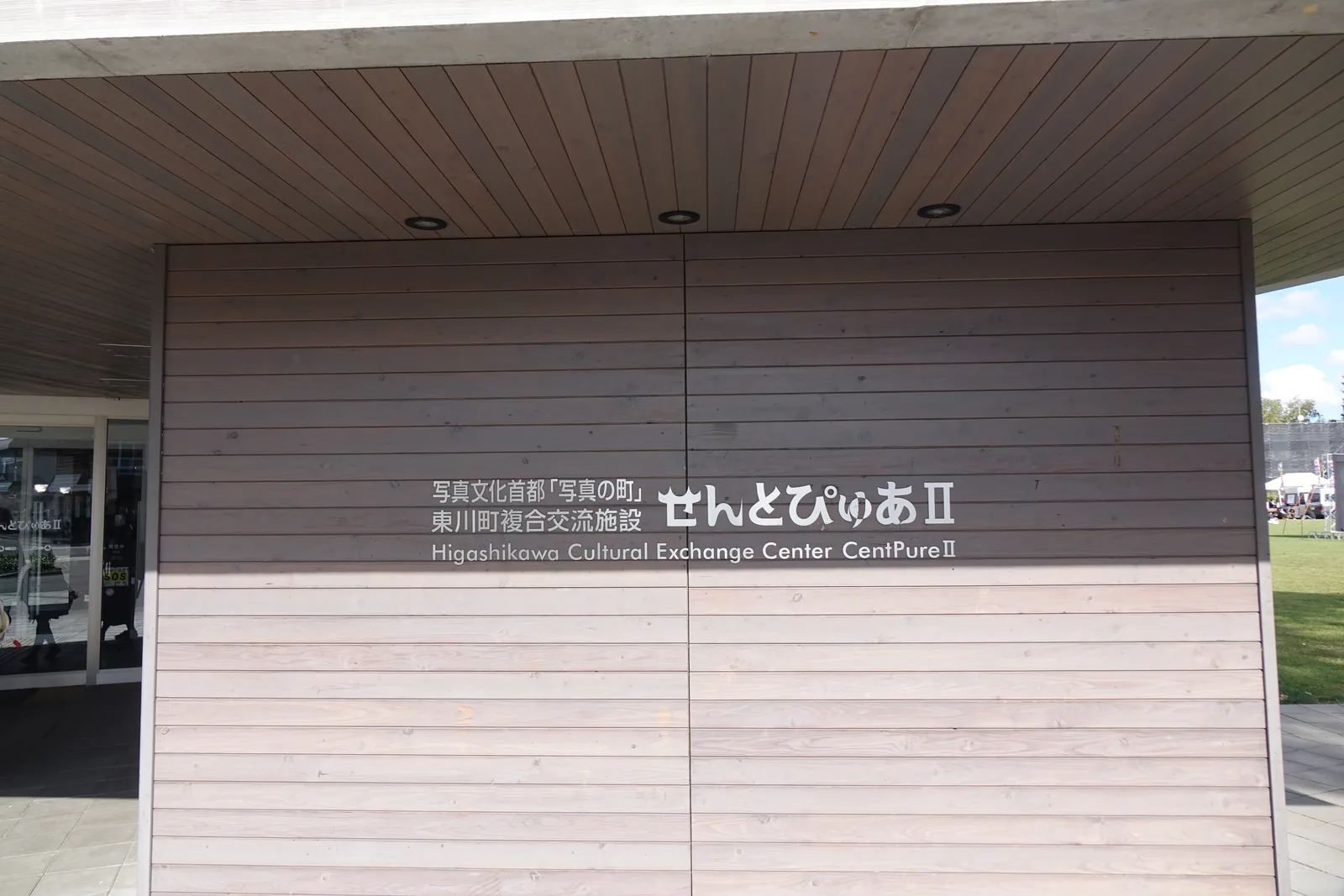 入口前的館名牆，深灰色橫向木板覆面，白字寫著館名與英文名稱，上方為同材質的雨庇底面