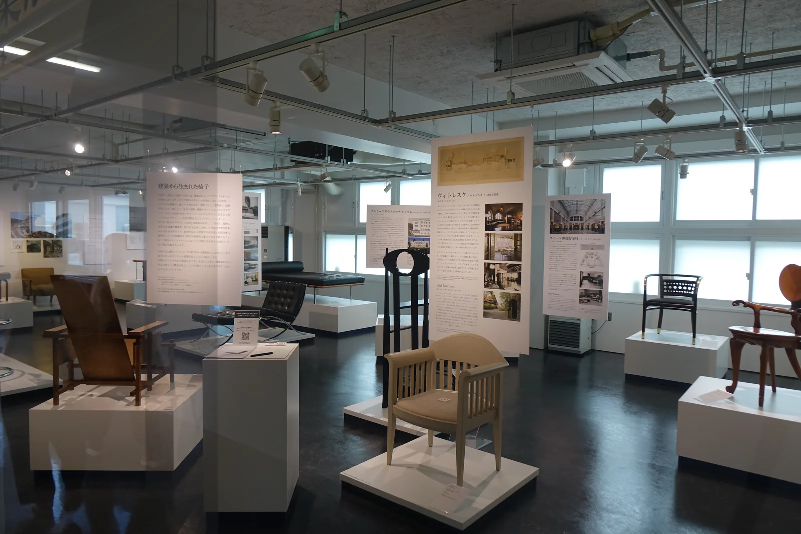 CentPure I畫廊，深色磨光地面上以白色台座展示多件設計名椅，後方為解說看板與舊校舍的窗戶
