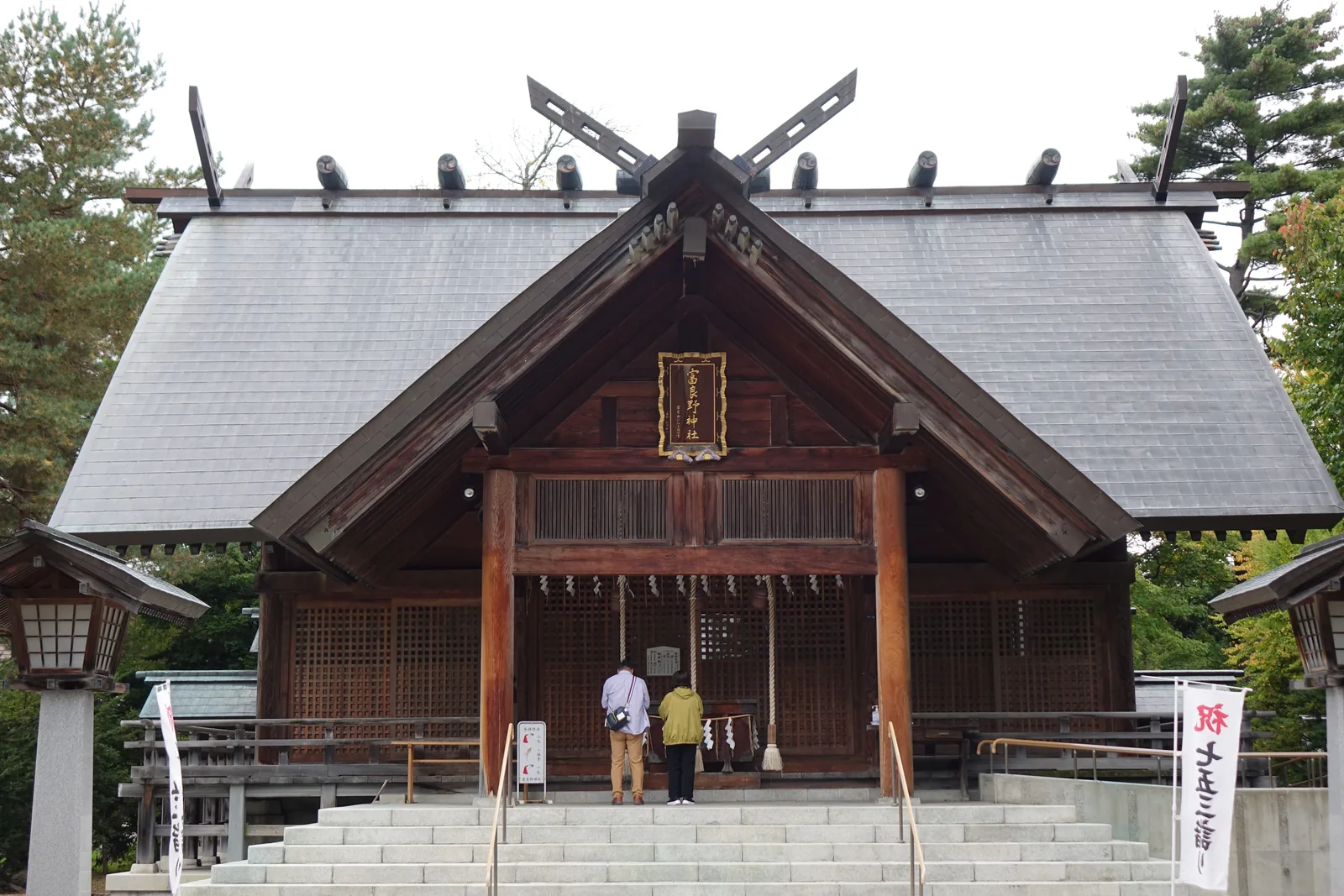 富良野神社社殿，切妻造屋頂上立著千木與鰹木，正面為木造的拜殿與石階，兩側為石燈籠與松樹