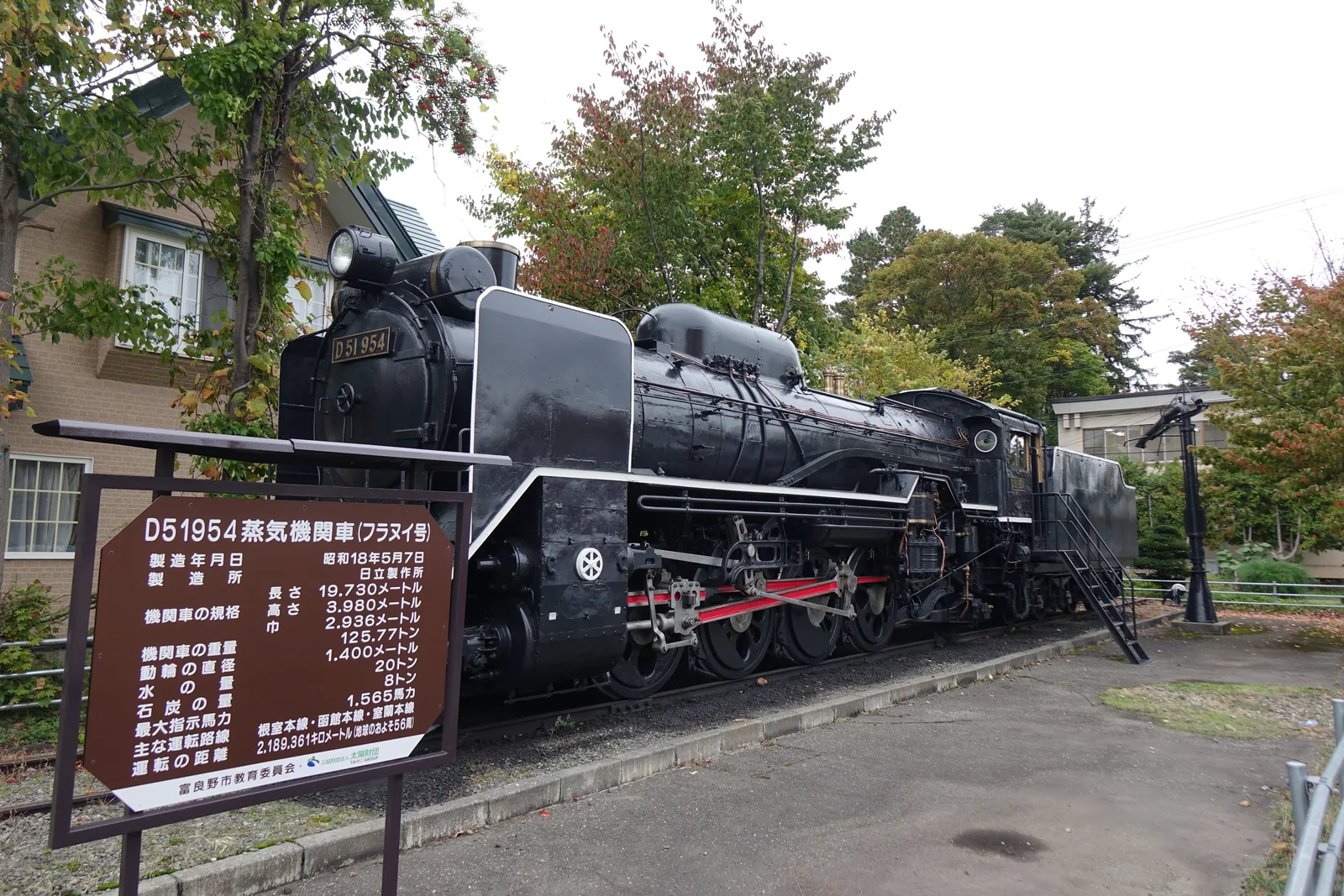路旁保存的D51型蒸汽機關車，黑色車身與紅色輪框，前方立著褐色的解說牌