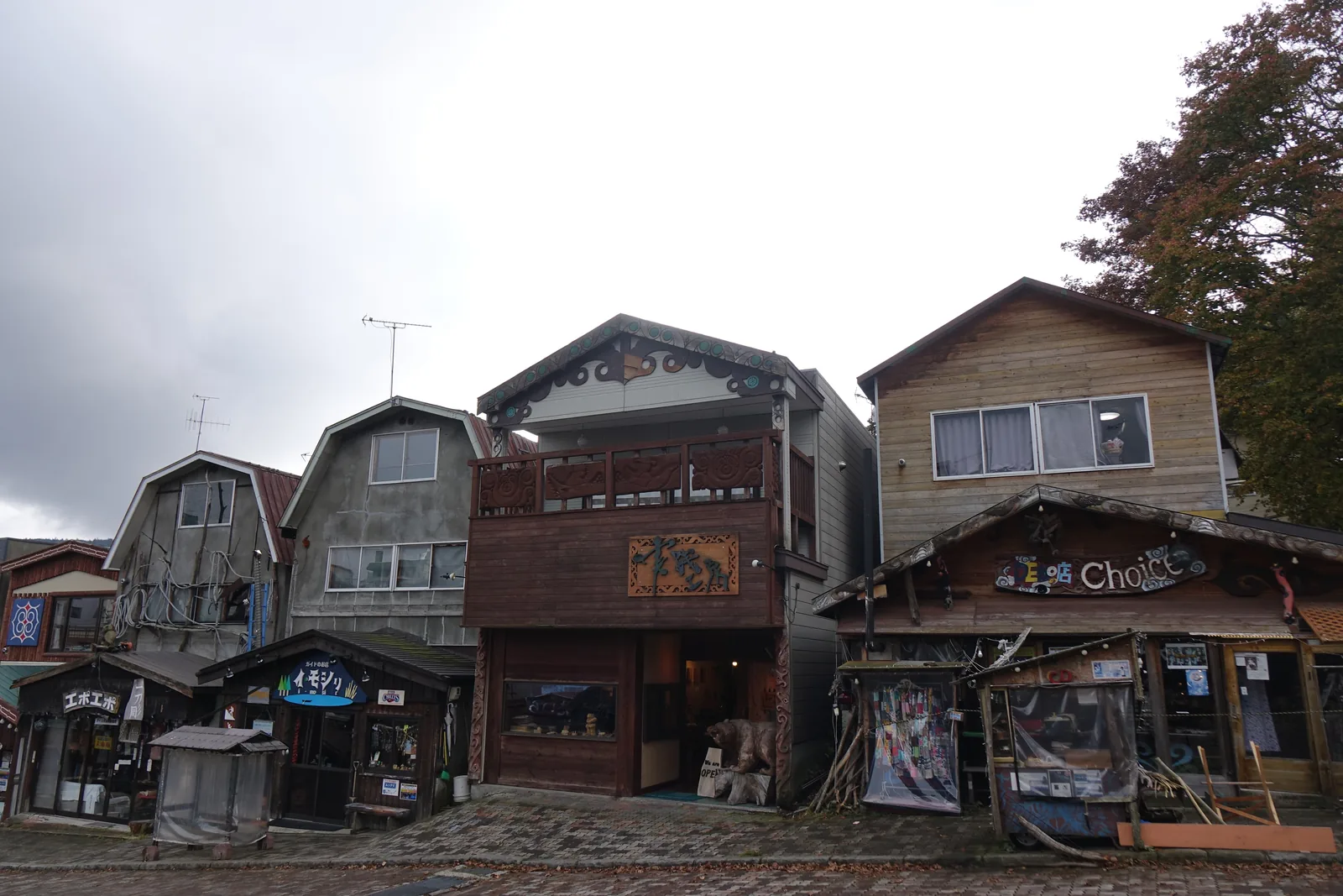 愛努聚落坡道一側的民藝店，數棟木造二至三層建築並排，一樓為店面，招牌上刻有動物與紋樣