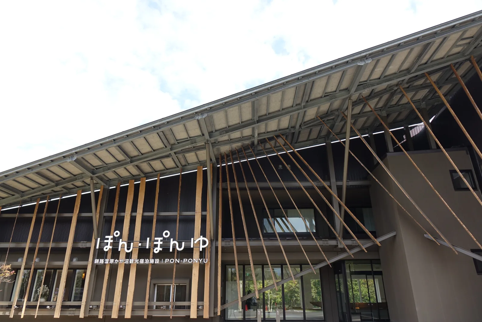 大簷底面，外露的鋼骨桁架與檁條，簷口懸掛細長的木材，木材斜向伸向地面，下方為館名與玻璃入口