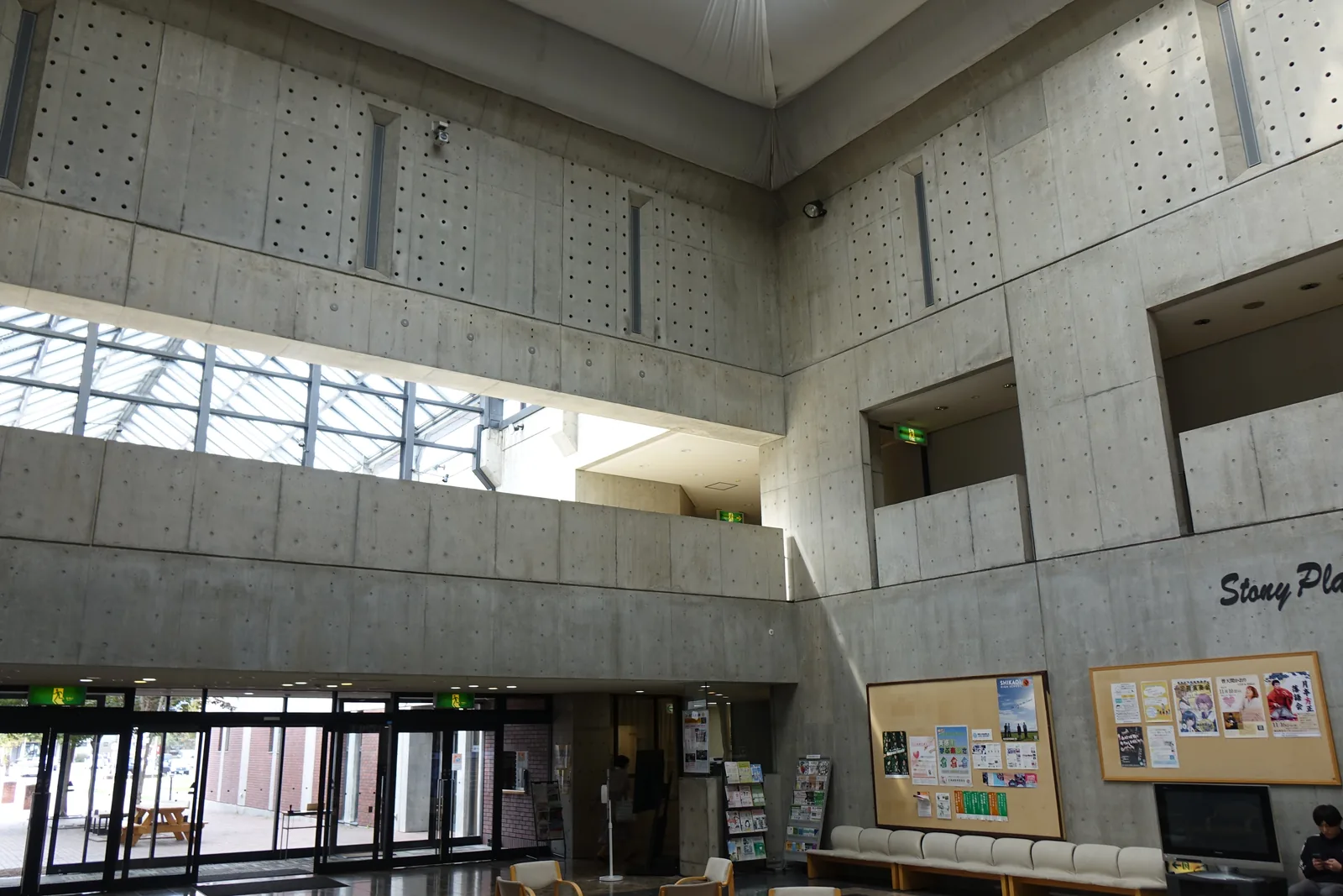 町民會館大廳上部，清水混凝土牆上規則排列模板孔，左側為鋼構的玻璃天窗帶，右側為二樓的方形開口，下方為通往戶外的玻璃門