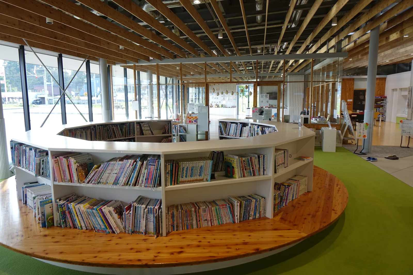 圓形書架與其後的玻璃立面，窗外為迴車道、停車場與遠方的山，窗框外可見斜撐