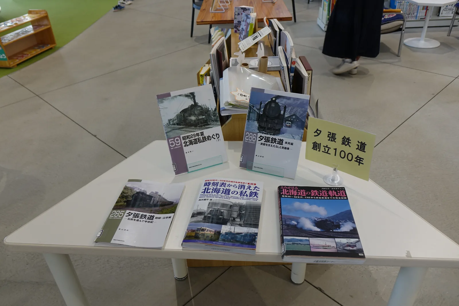 桌上陳列的鐵道書籍，封面為蒸汽機車與舊時的鐵道照片，中央立牌寫著夕張鐵道創立百年