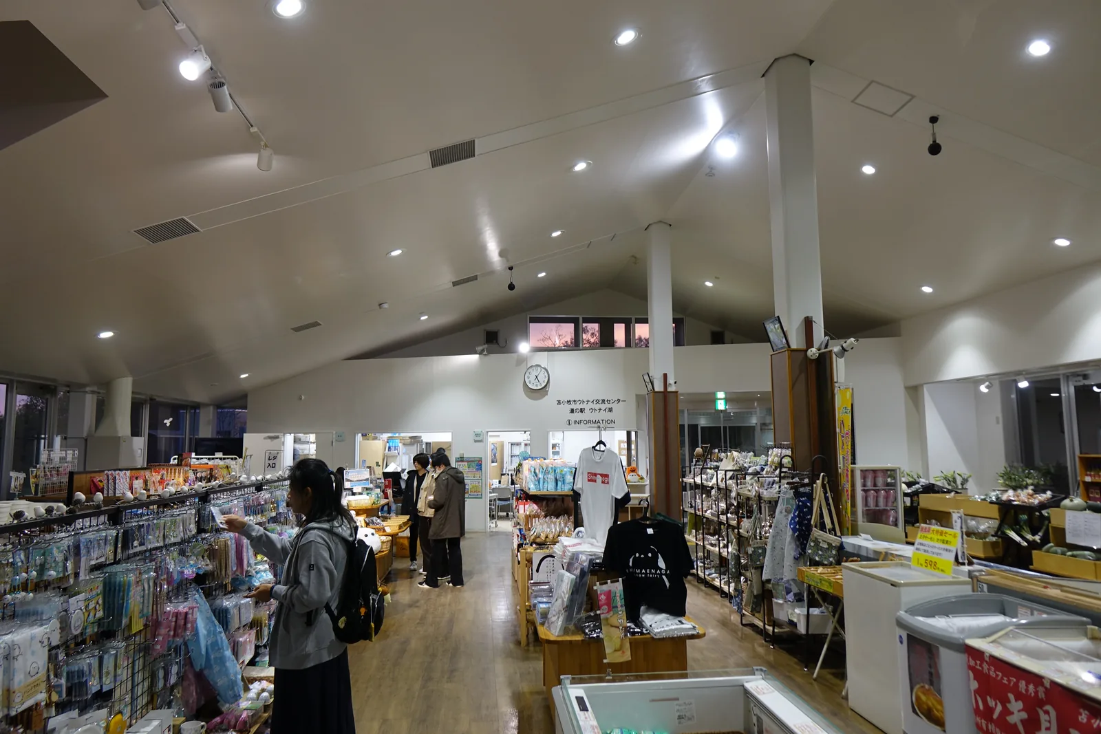 交流中心的商店內部，白色的山形天花下立著白色圓柱，柱的下半段以木材包覆，兩側為商品架與冷凍櫃，深處為詢問處