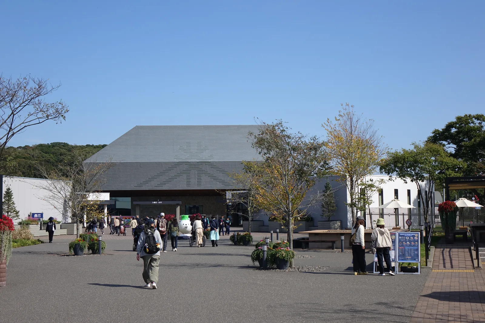歡迎廣場，正面為入口棟與其後博物館的灰色量體，廣場上為步道、植栽與參觀者