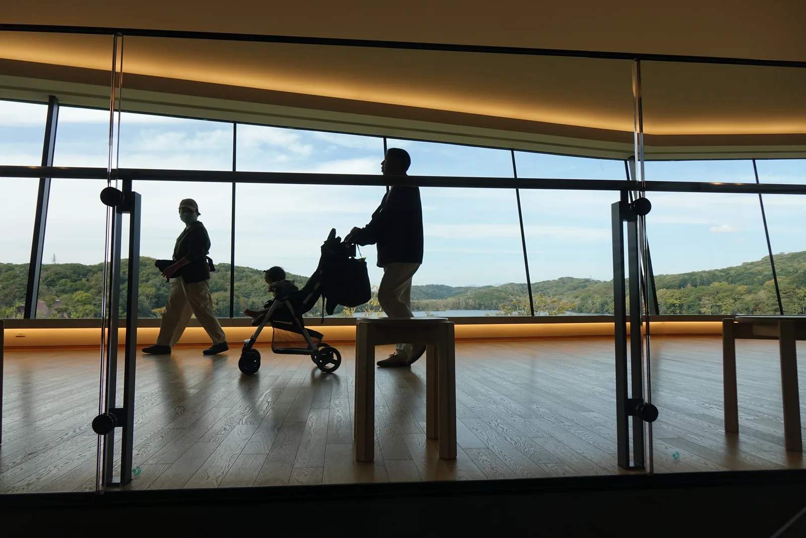 Panoramic Lobby，向外傾斜的整面玻璃外為 Poroto 湖與對岸的丘陵，窗台下緣為暖色的間接照明，前方為木凳與橡木地板