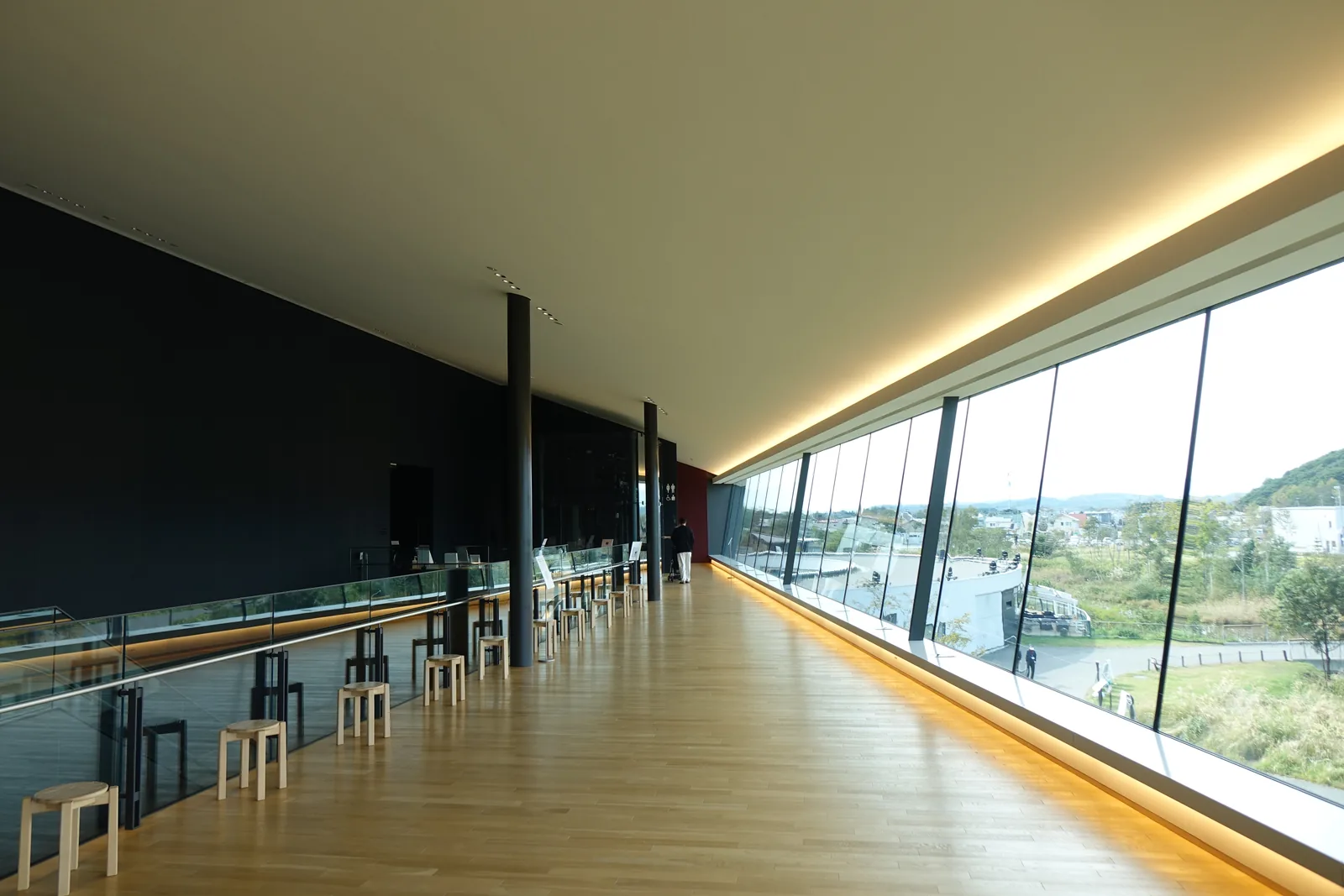 Panoramic Lobby 的長向，左側為深色的牆面與細柱，右側為一路延伸的傾斜玻璃，窗外為園區與丘陵