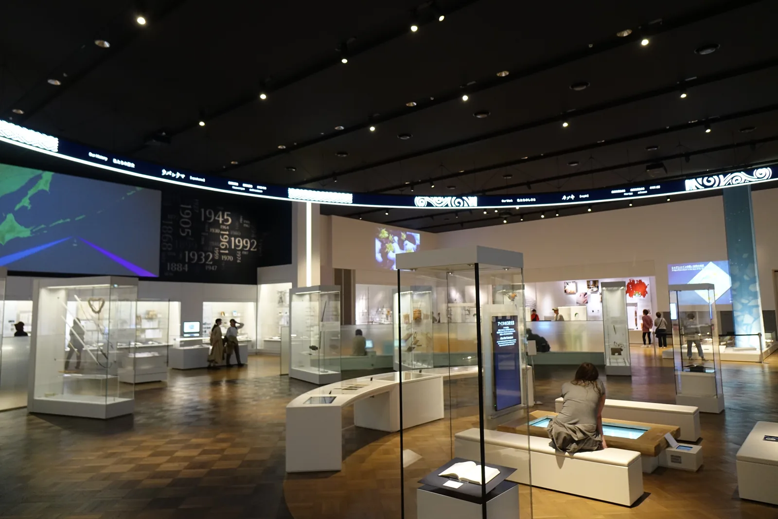 離開展示室的幽暗走廊，兩側為深色牆面，盡頭為明亮的開口與玻璃外的景色