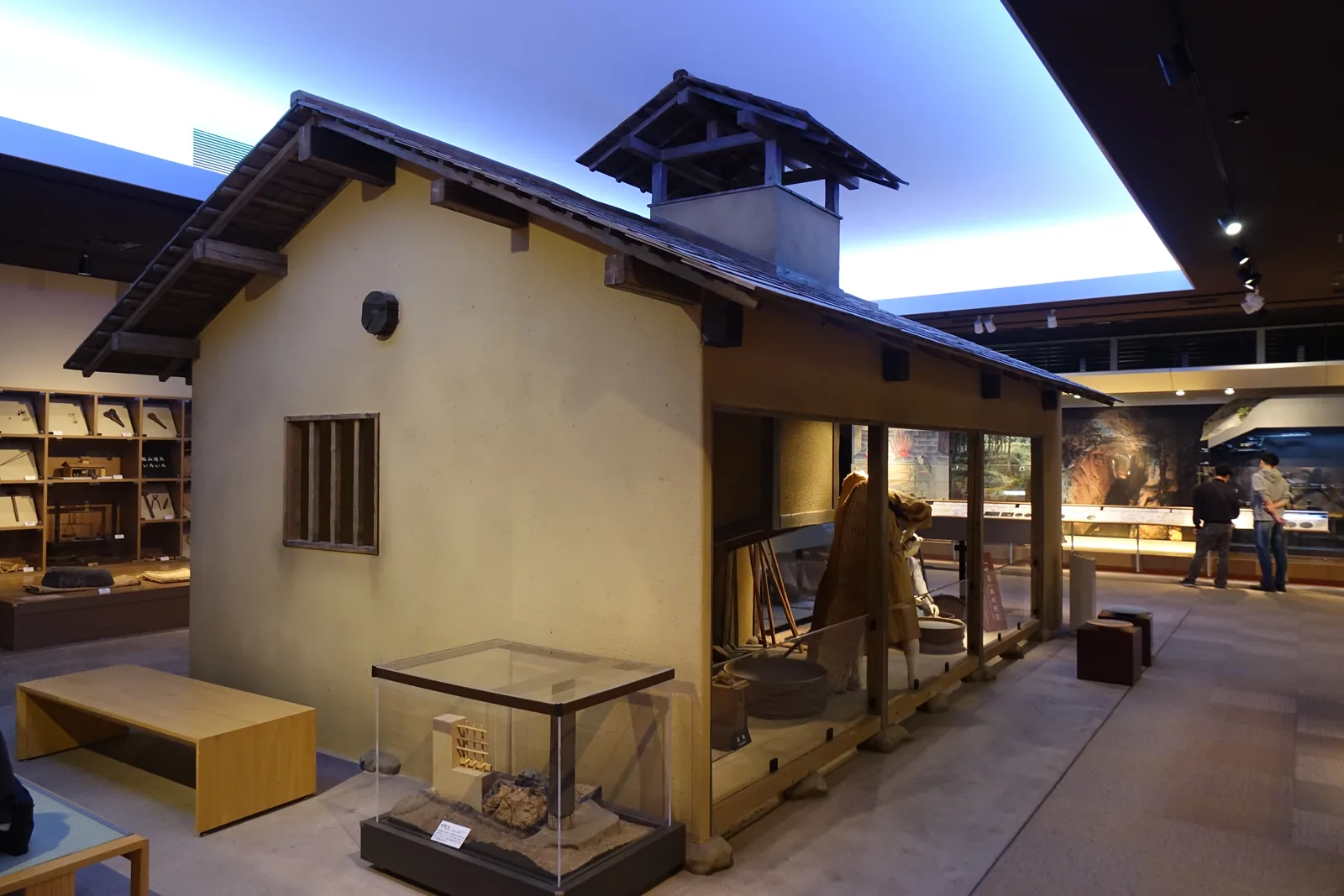 展示室中再現的吹屋，一棟土牆、木格窗、瓦葺屋頂的小屋，屋脊上另起一座排煙用的小屋頂，屋簷下是半開放的作業空間與人形，上方的天花板是一片發光的面，前方是一張木長凳與玻璃展示櫃