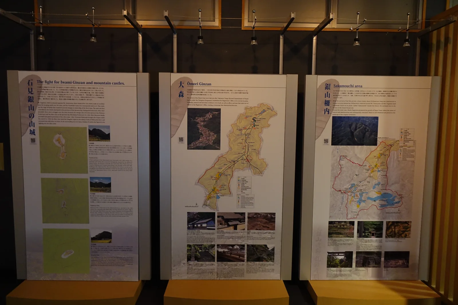 第四展示室，三片並排的大型看板分別介紹石見銀山的山城、大森與銀山柵內，看板上方是木製的吊架與燈具
