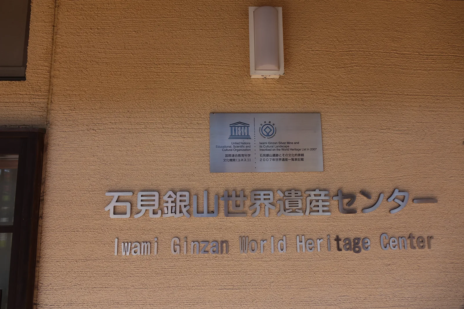 淺褐色的土壁上固定著不鏽鋼字的館名與英文名，上方是一塊標示世界遺產與聯合國教科文組織的金屬銘板與一盞壁燈